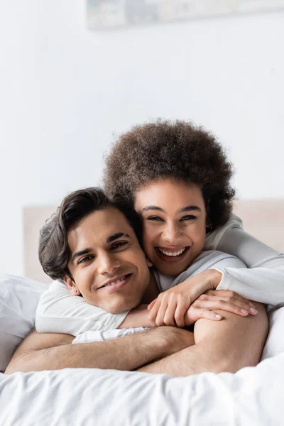 Heureux interracial couple souriant tout en étreignant sur lit — Photo de stock