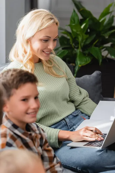 Smiling mother writing in notebook near blurred kids at home — Stock Photo