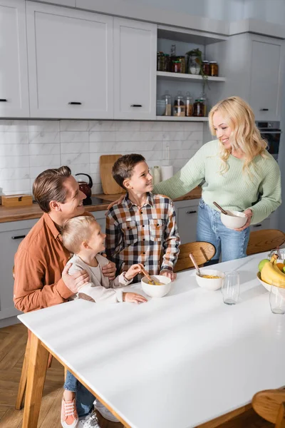 Homme heureux avec des enfants prendre le petit déjeuner tout en regardant mère avec bol — Photo de stock