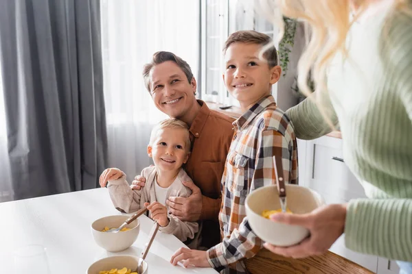 Happy family with bows of corn flakes having breakfast in kitchen — Stock Photo