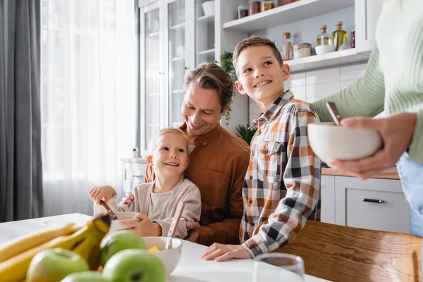 Father with boys having breakfast near blurred fruits and mother with bowl — Stock Photo