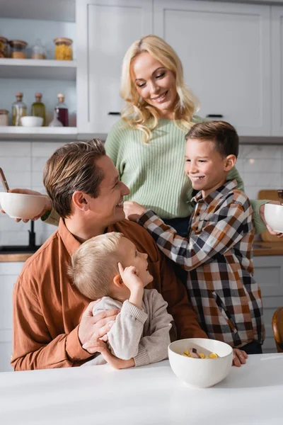 Famille heureuse regardant mère pendant le petit déjeuner dans la cuisine — Photo de stock