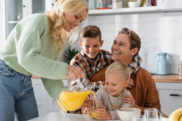 Femme heureuse versant du jus d'orange frais pendant le petit déjeuner en famille — Photo de stock