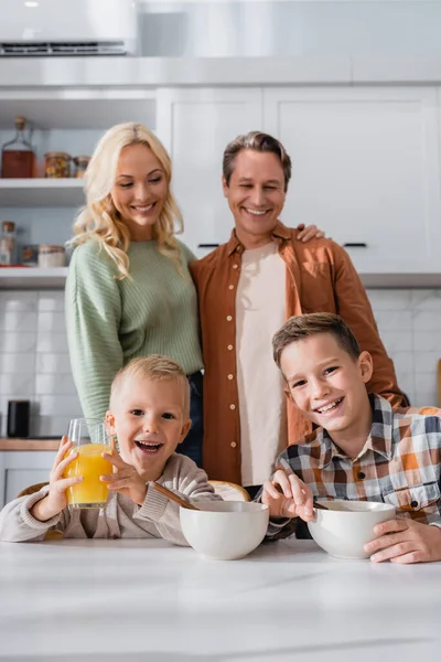 Mari heureux et femme debout près de fils prenant le petit déjeuner dans la cuisine — Photo de stock
