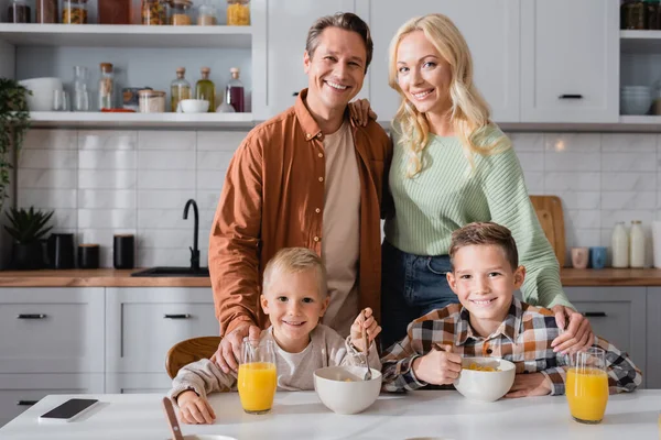 Famille heureuse regardant la caméra pendant le petit déjeuner dans la cuisine — Photo de stock