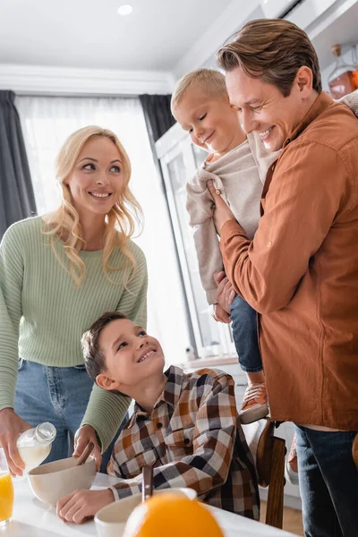 Smiling man holding kid while wife pouring milk for breakfast — Stock Photo