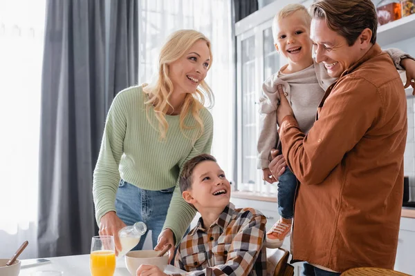 Woman pouring milk into bowl near family in kitchen — Stock Photo