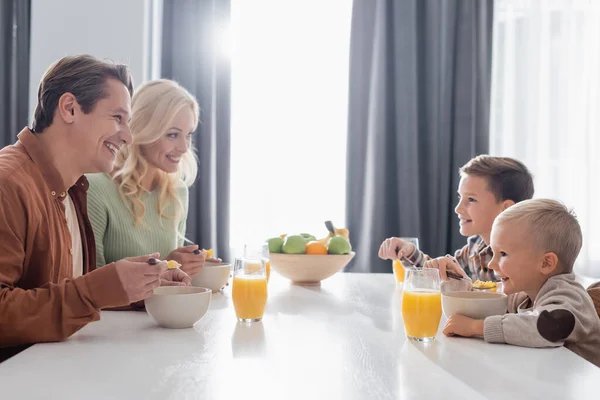 Parents heureux et fils parlent tout en mangeant des flocons de maïs savoureux pour le petit déjeuner — Photo de stock