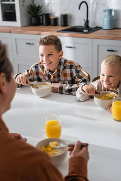 Cheerful boys eating tasty corn flakes near blurred father in kitchen — Stock Photo