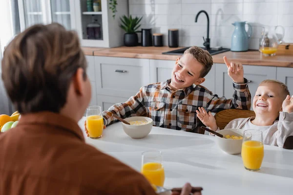 Fröhliche Jungen gestikulieren beim Frühstück mit Papa im verschwommenen Vordergrund — Stockfoto