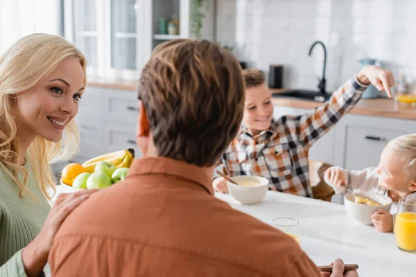 Rückansicht eines verschwommenen Mannes neben glücklicher Frau und Söhnen am Küchentisch — Stockfoto