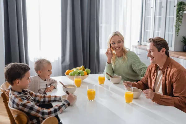 Smiling woman talking on smartphone during breakfast with husband and sons — Stock Photo