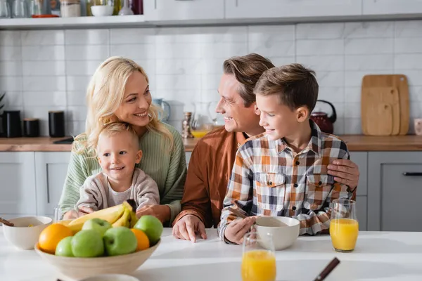 Happy couple embracing kids during breakfast near fresh fruits and orange juice — Stock Photo