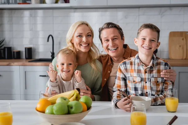 Padres felices e hijos sonriendo a la cámara mientras desayunan en la cocina - foto de stock