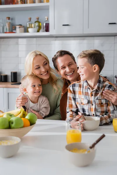 Genitori allegri che abbracciano i bambini mentre fanno colazione in cucina — Foto stock