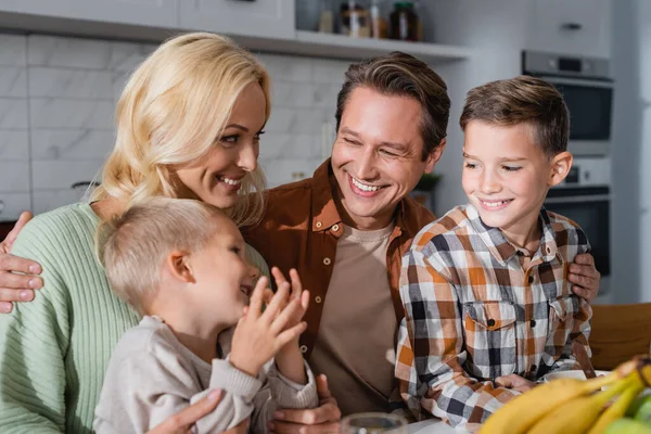 Jubelnde Familie blickt auf kleinen Jungen neben verschwommenen Bananen in Küche — Stockfoto