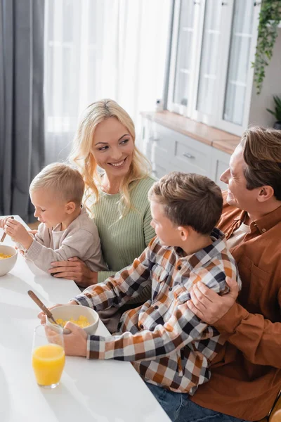 Радісний чоловік і жінка дивляться один на одного біля синів їдять кукурудзяні пластівці на сніданок — стокове фото