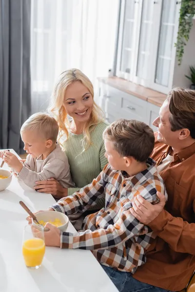 Freudiger Mann und Frau, die sich in der Nähe von Söhnen beim Frühstück mit Cornflakes betrachten — Stockfoto