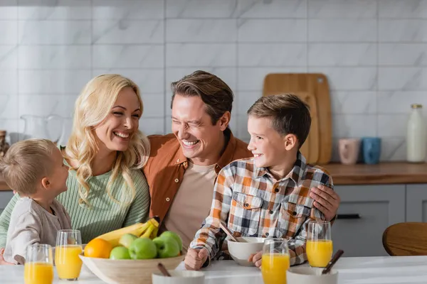 Heureux famille rire dans la cuisine près de verres avec du jus d'orange et bol avec des fruits frais — Photo de stock