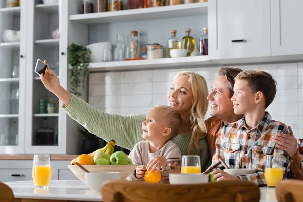 Щаслива жінка бере селфі на мобільний телефон, снідаючи з сім'єю — стокове фото
