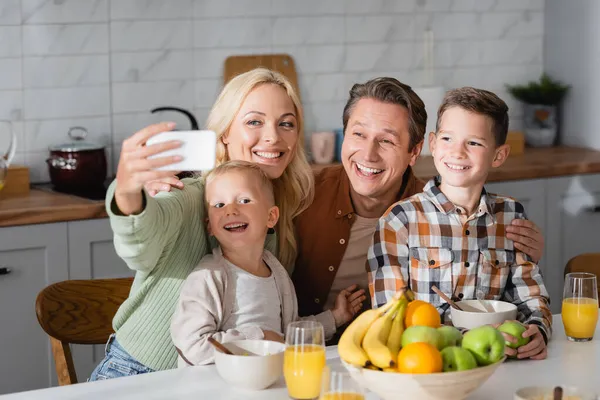 Счастливая женщина делает селфи на мобильный телефон во время завтрака с семьей — стоковое фото