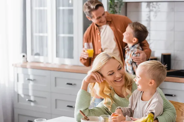 Cheerful woman looking at kid near husband and son on blurred bckground — Stock Photo