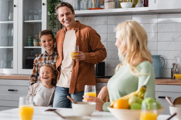 Homme avec fils près de femme floue assis à la table de cuisine près du petit déjeuner — Photo de stock