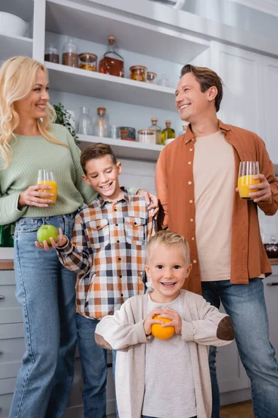 Parents with orange juice and boys with oranges smiling in kitchen — Stock Photo