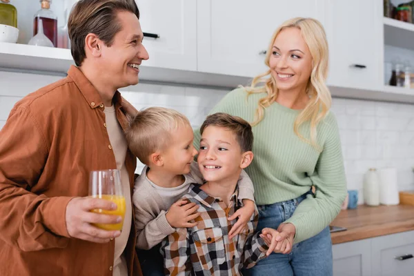 Marido feliz e esposa olhando uns para os outros perto de filhos alegres abraçando na cozinha — Fotografia de Stock