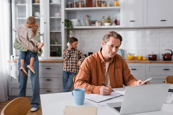 Boy talking on mobile phone near mom, brother and dad working in kitchen — Stock Photo
