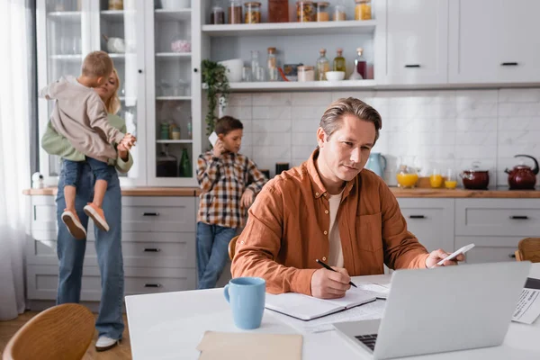 Garçon parlant sur téléphone mobile près de maman, frère et père travaillant dans la cuisine — Photo de stock