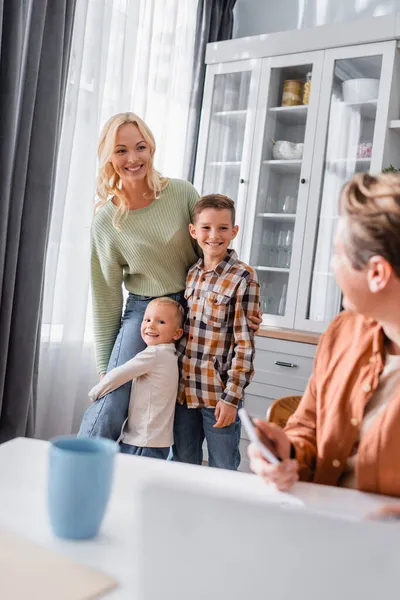 Mujer feliz con los niños cerca del hombre borroso que trabaja en la cocina en primer plano borrosa - foto de stock