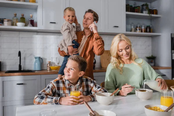 Man holding kid and pouring milk in corn flakes during breakfast in kitchen — Stock Photo