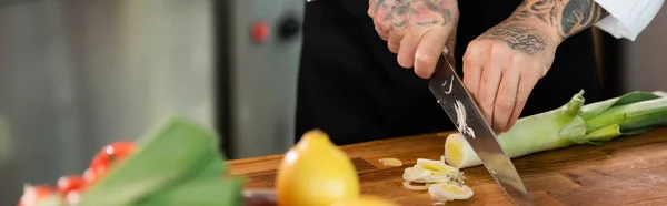 Ausgeschnittene Ansicht des Chefs, der Porree in der Nähe von verschwommenem Gemüse in der Küche schneidet, Banner — Stockfoto
