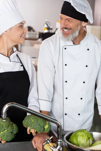 Cuochi positivi che tengono verdure vicino al rubinetto nella cucina del ristorante — Foto stock