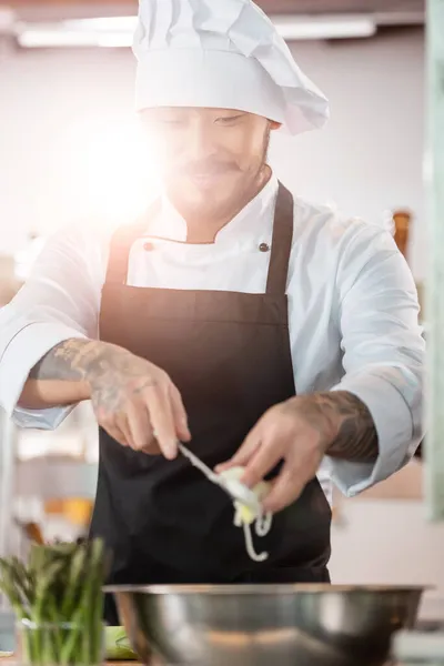 Sorrindo asiático chef segurando em fatias alho-porro perto tigela na cozinha — Fotografia de Stock