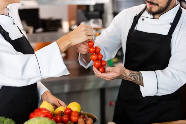 Обрізаний вид шеф-кухарів в фартухах, що тримають вишневі помідори на кухні — стокове фото