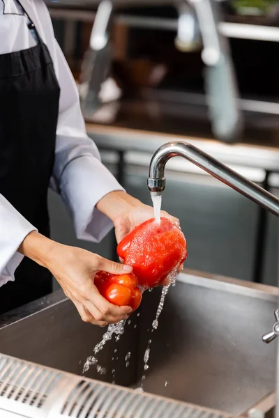 Cropped view of chef washing bell peppers in kitchen — Stock Photo