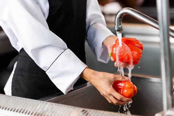 Cropped view of chef washing bell peppers near faucet in kitchen — Stock Photo