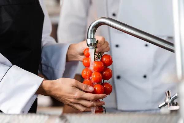 Vue recadrée du chef qui lave les tomates cerises près d'un collègue flou dans la cuisine — Photo de stock