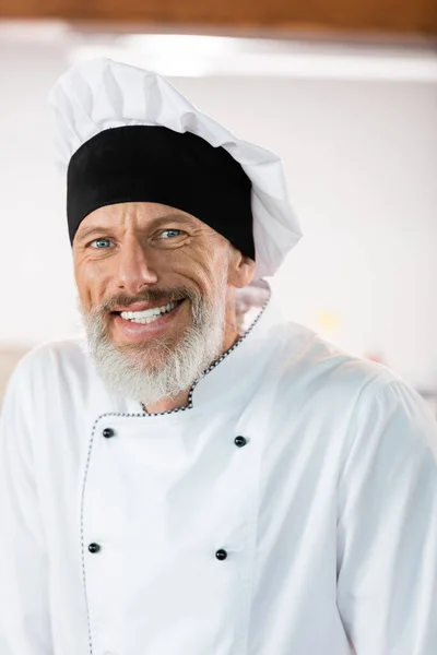 Happy chef in uniform looking at camera in kitchen — Stock Photo