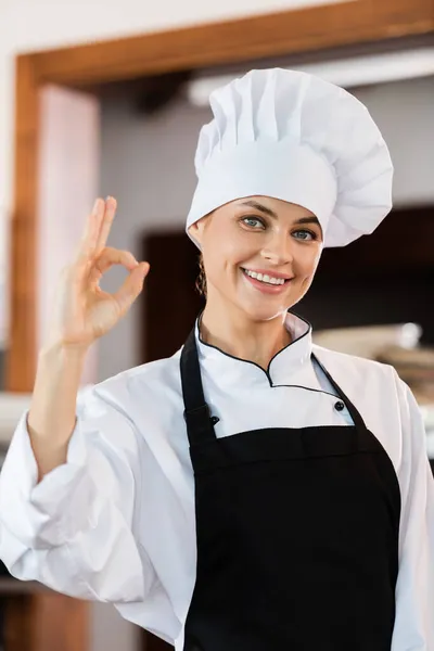 Chef positif en casquette et tablier montrant un geste correct dans la cuisine — Photo de stock