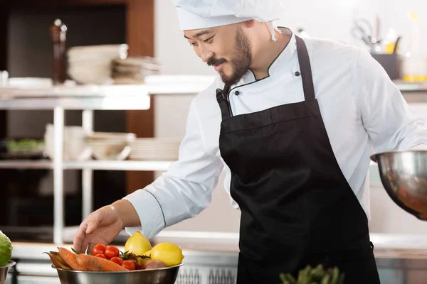 Chef asiatique dans tablier regardant les légumes frais dans la cuisine du restaurant — Photo de stock