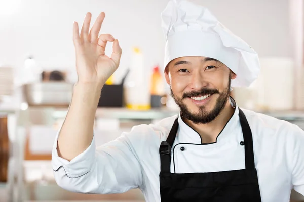 Ritratto di sorridente cuoco asiatico in uniforme mostrando il gesto giusto in cucina — Foto stock