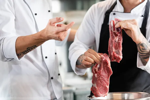 Vue recadrée du chef pointant du doigt la viande dans les mains d'un collègue dans la cuisine — Photo de stock