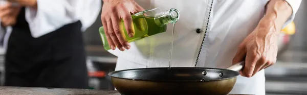 Обрізаний вид шеф-кухаря наливає оливкову олію на сковороду на кухню, банер — стокове фото