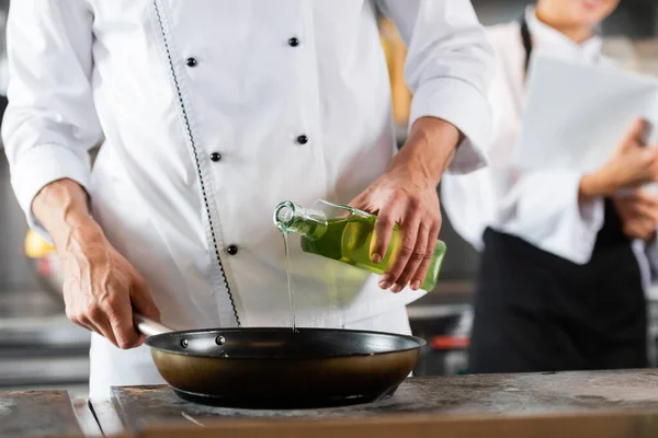 Ausgeschnittene Ansicht des Chefs, der in der Küche Olivenöl auf Pfanne auf Kochplatte gießt — Stockfoto