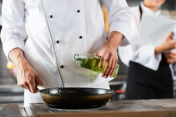 Vista cortada do chef derramando azeite na frigideira no fogão na cozinha — Fotografia de Stock