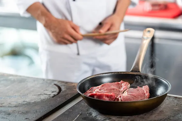 Обрезанный вид сырого мяса на сковороде рядом с размытым шеф-поваром на кухне — стоковое фото