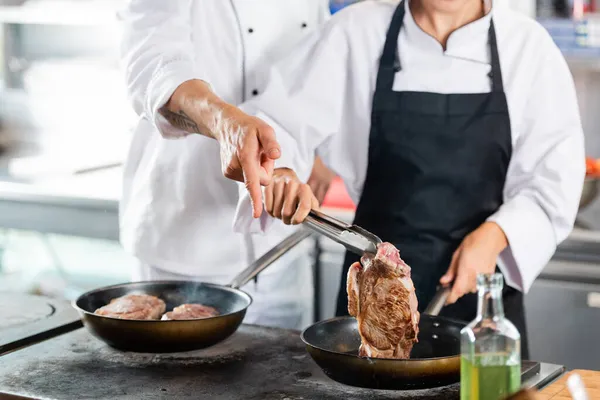 Cropped view of chef pointing with finger near colleague cooking meat and olive oil in kitchen — Stock Photo